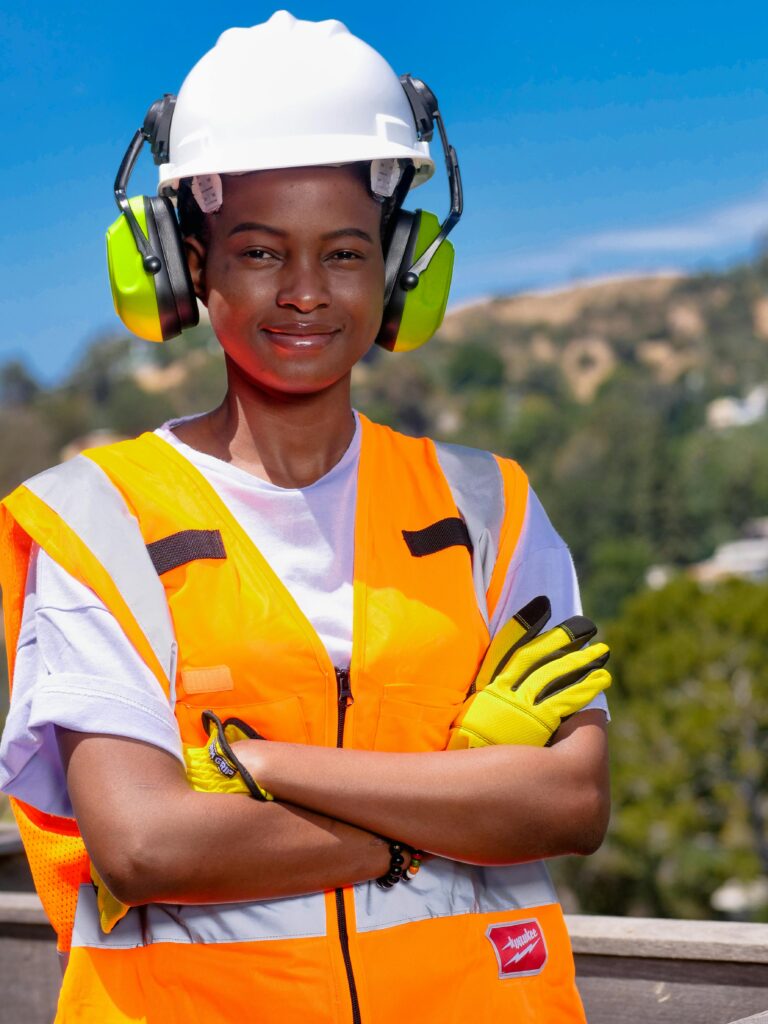 Smiling female engineer wearing PPE and hardhat on a sunny day outdoors.